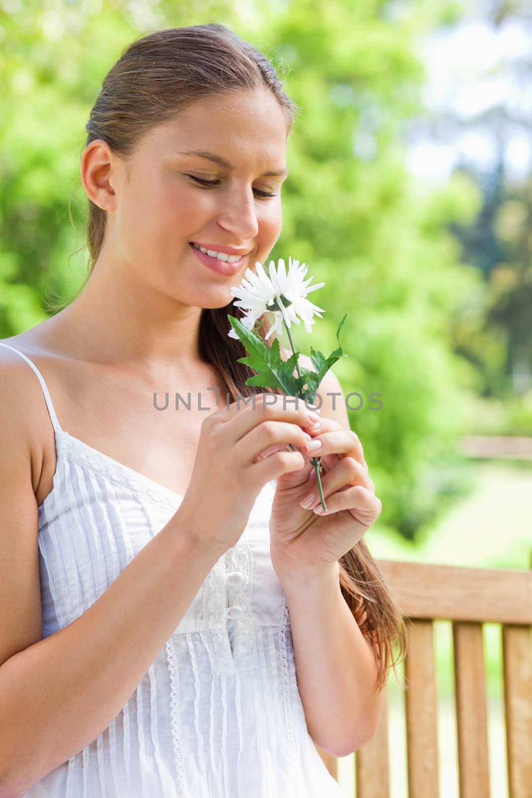 Smiling young woman on a park bench smelling on a flower