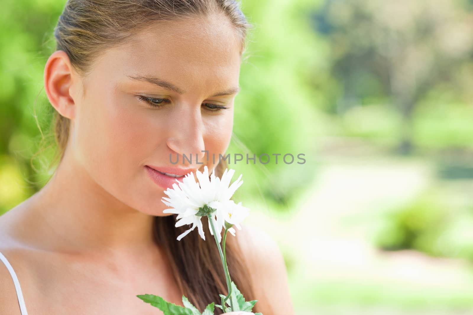 Young woman smelling on a white flower in the park