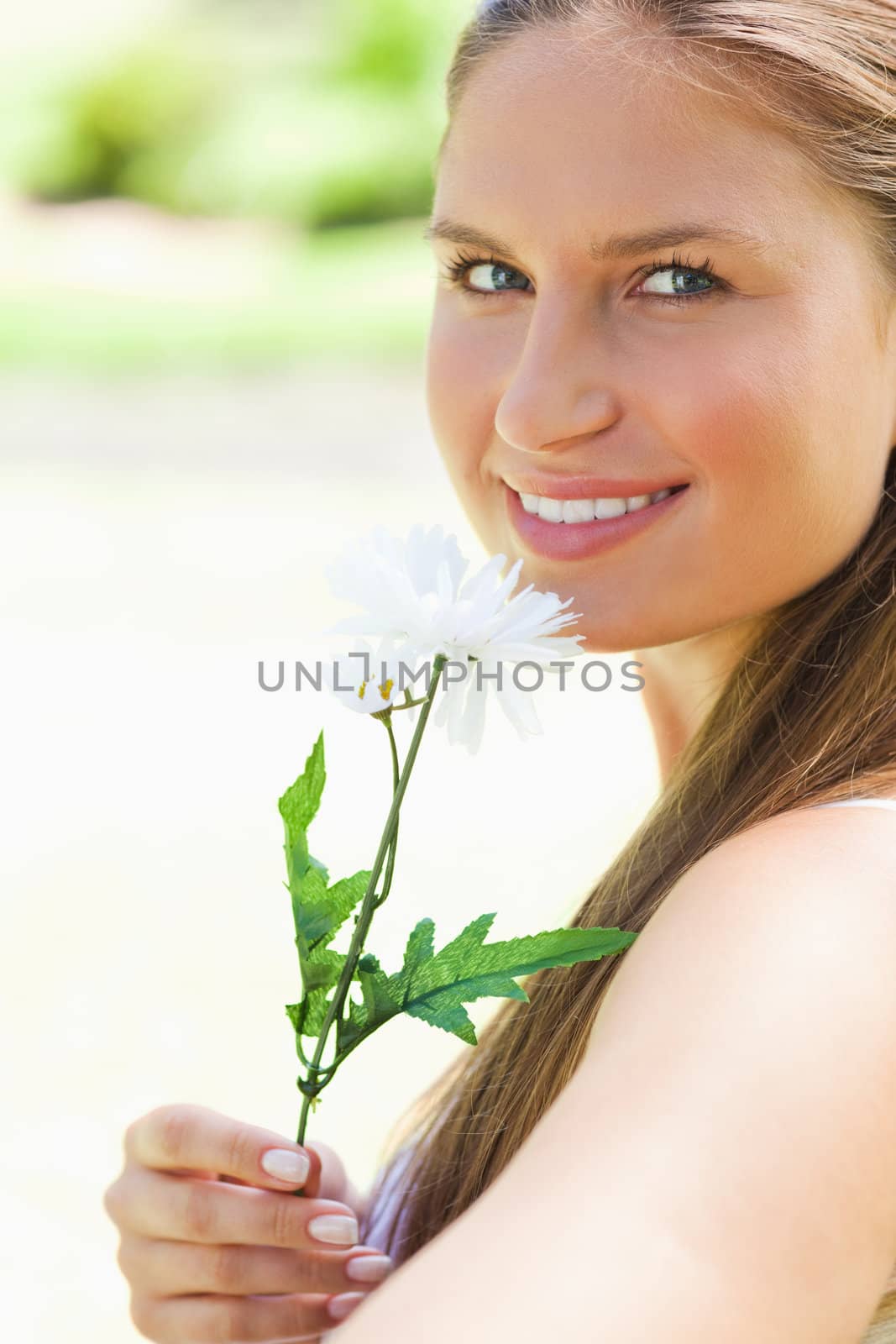 Close up of a smiling young woman smelling a flower