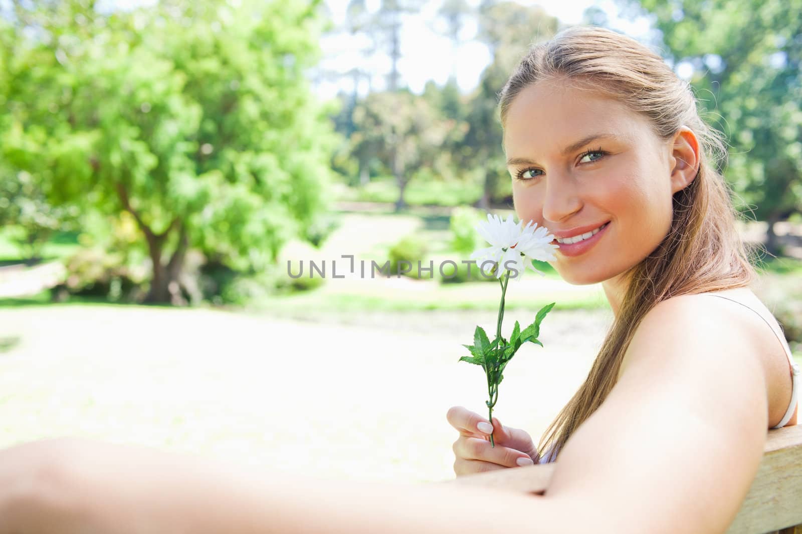 Side view of a smiling young woman smelling a flower in the park