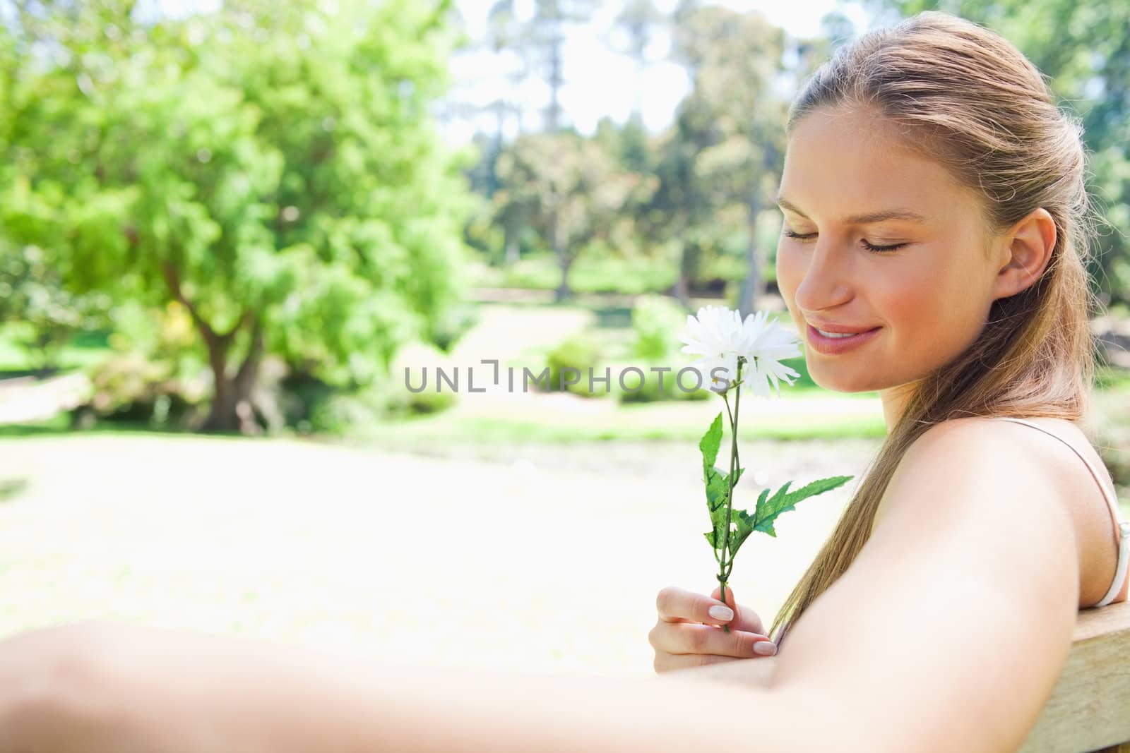 Side view of a young woman on a park bench smelling a flower