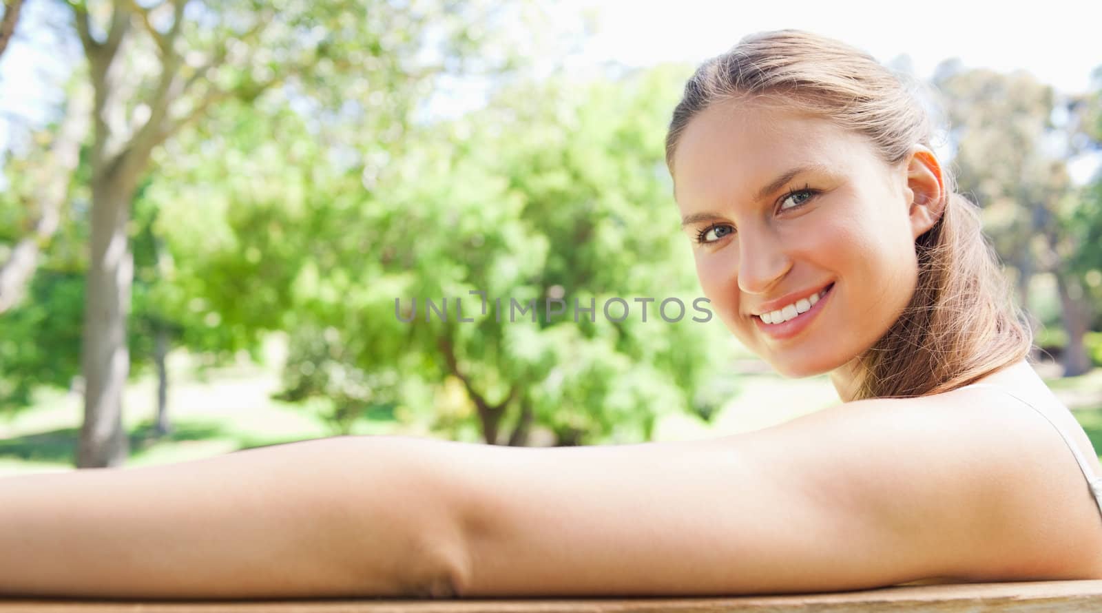 Side view of a smiling young woman sitting on a park bench