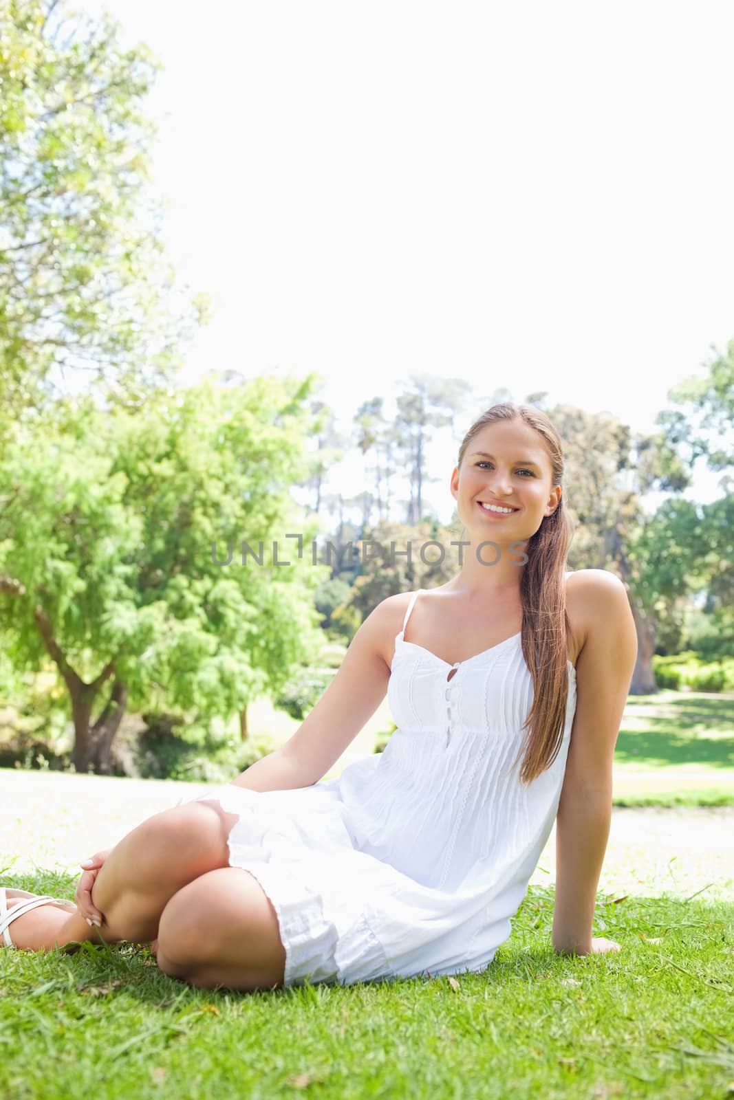 Smiling woman in the park sitting on the lawn by Wavebreakmedia