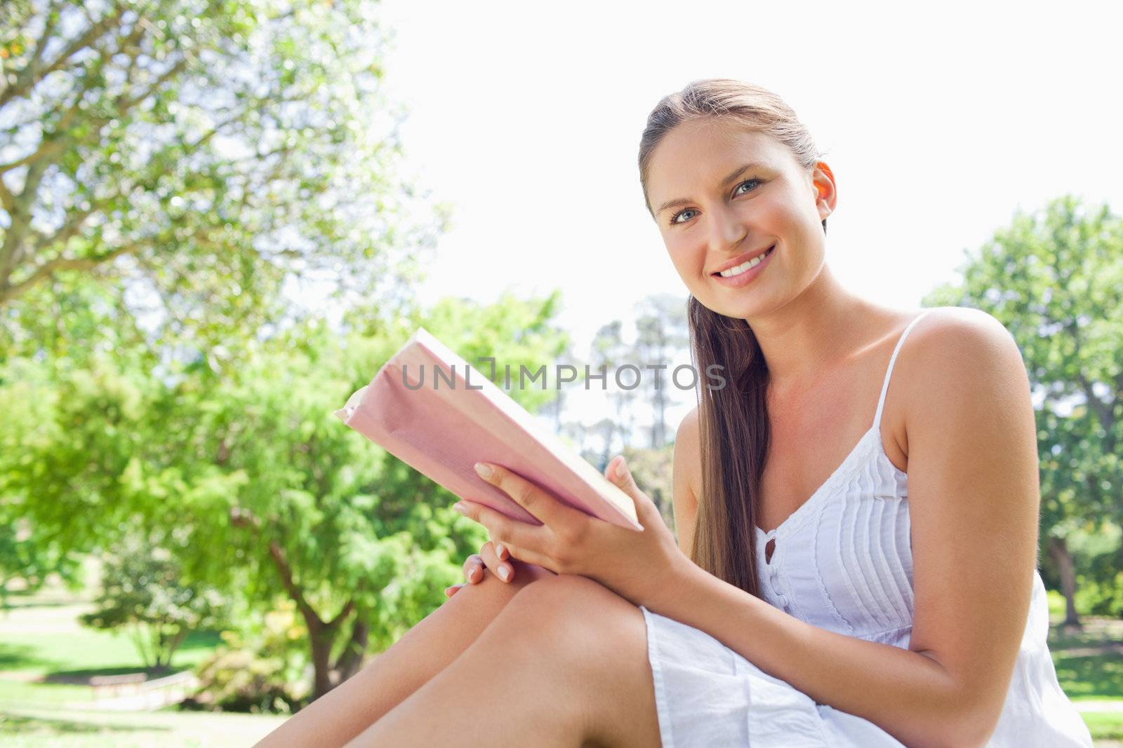 Side view of a smiling young woman with a book on the lawn