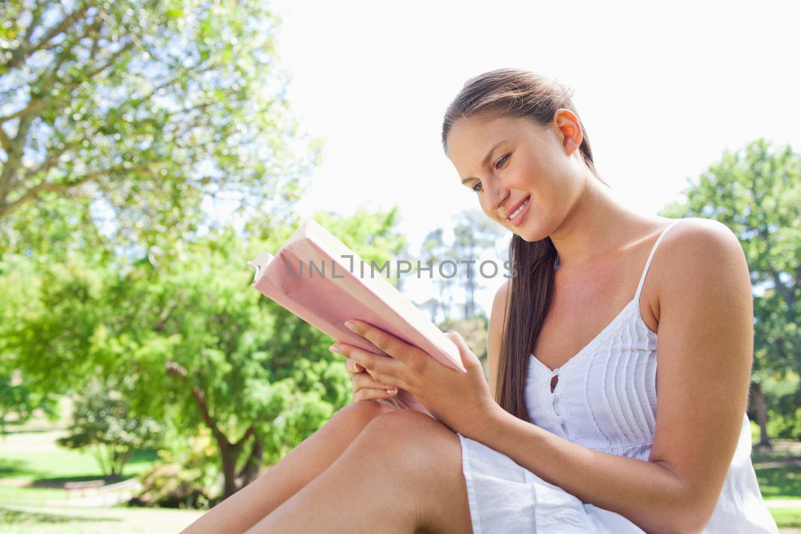 Side view of a smiling woman on the lawn reading a book by Wavebreakmedia