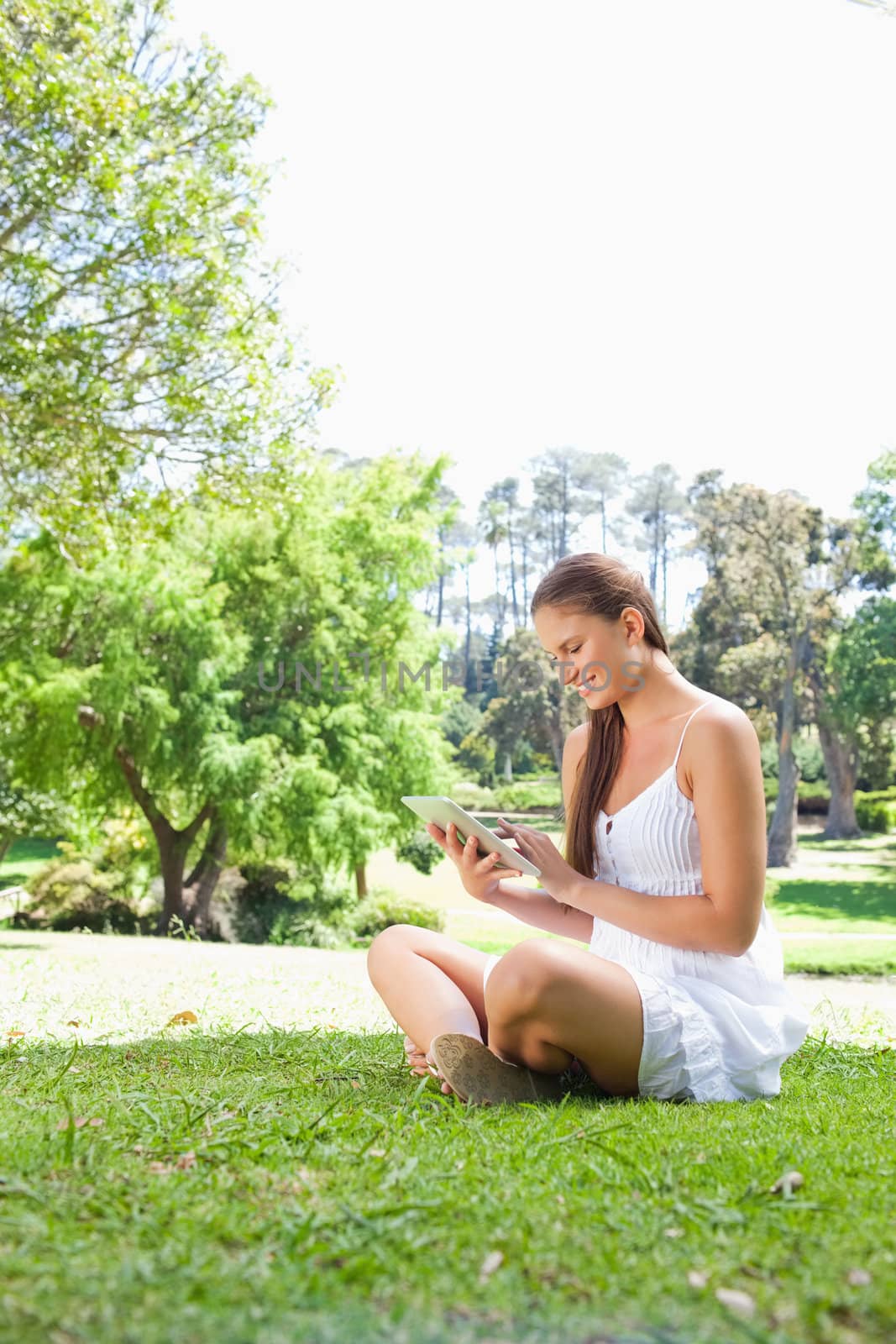 Side view of a smiling young woman on the lawn with a tablet computer