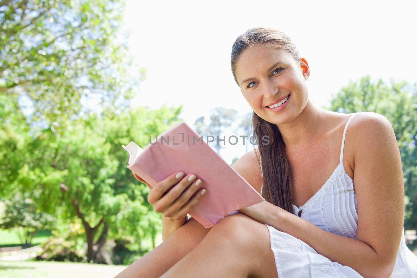 Side view of a smiling young woman with a novel in the park