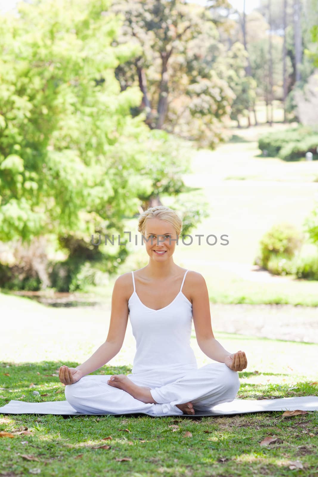 Smiling young woman sitting in a yoga position in the park