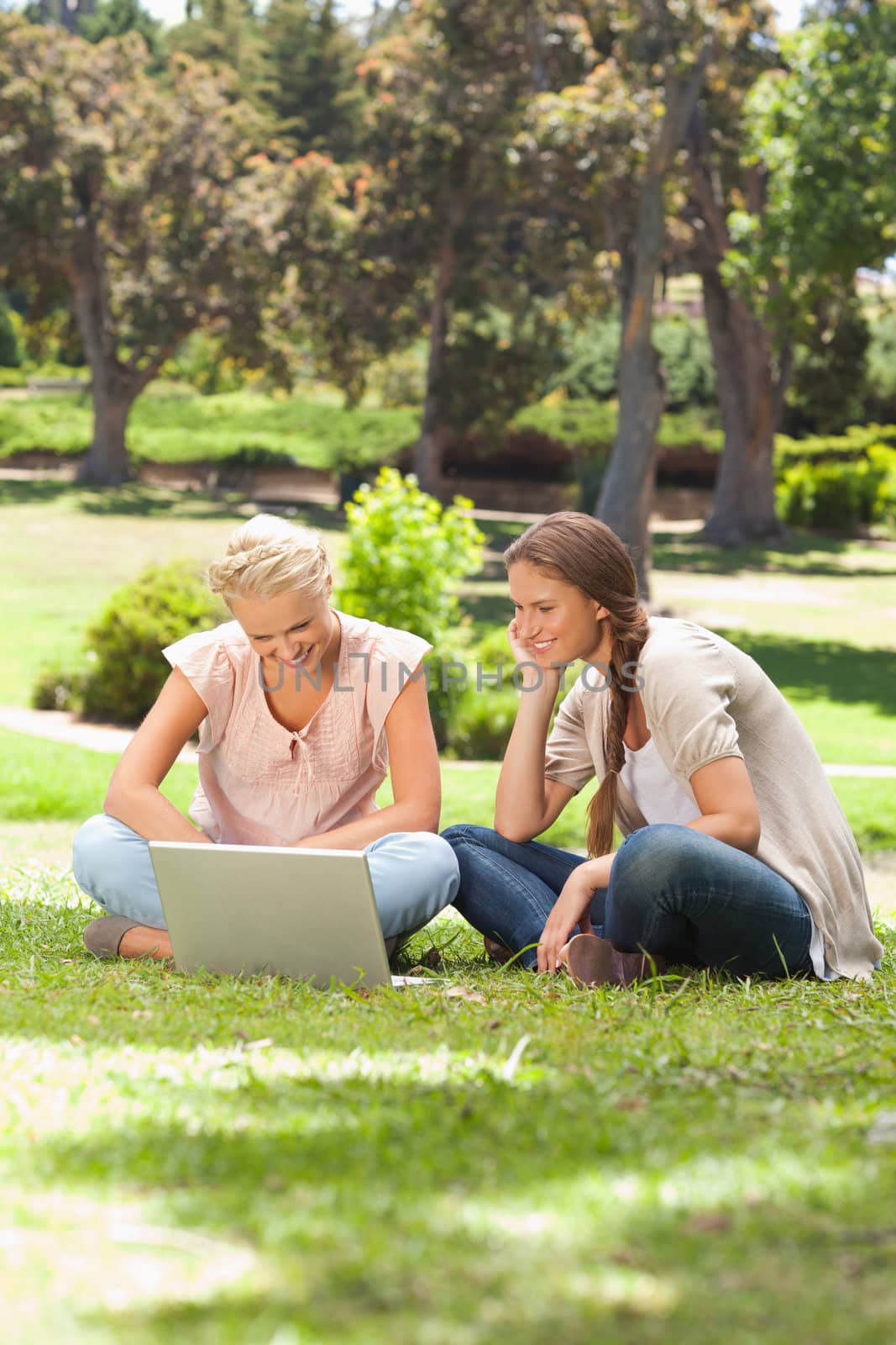 Smiling friends with a laptop sitting on the lawn by Wavebreakmedia