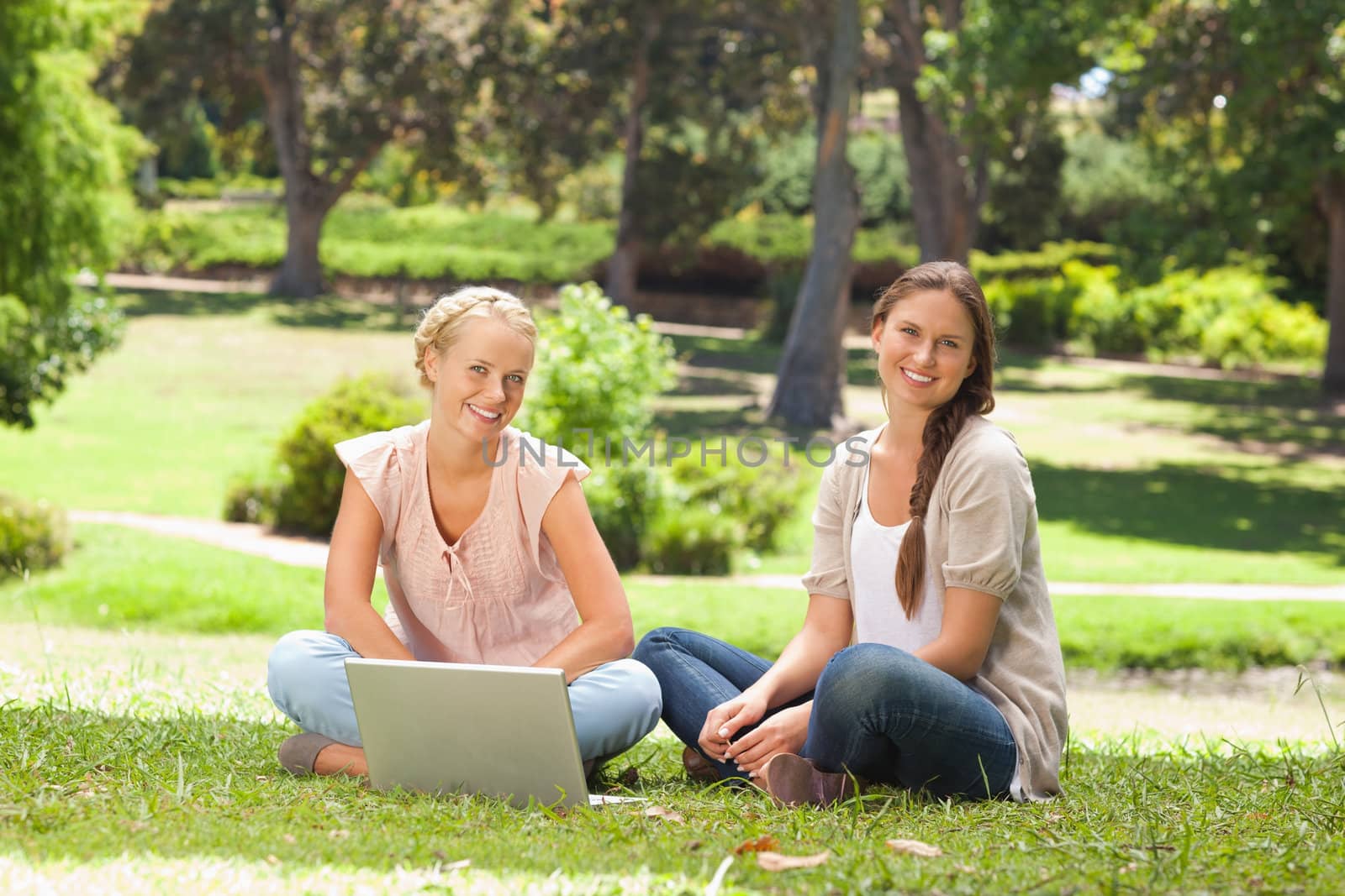 Smiling young women sitting in the park with a laptop