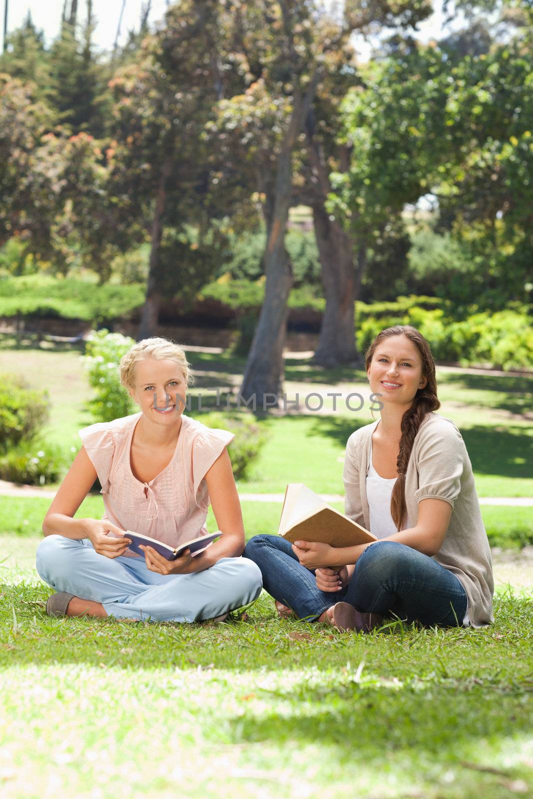 Smiling young women with their books sitting in the park
