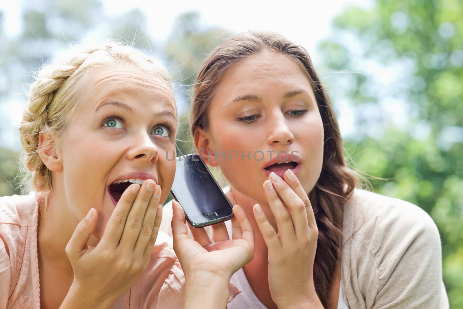 Curious female friends listening to phone call in the park