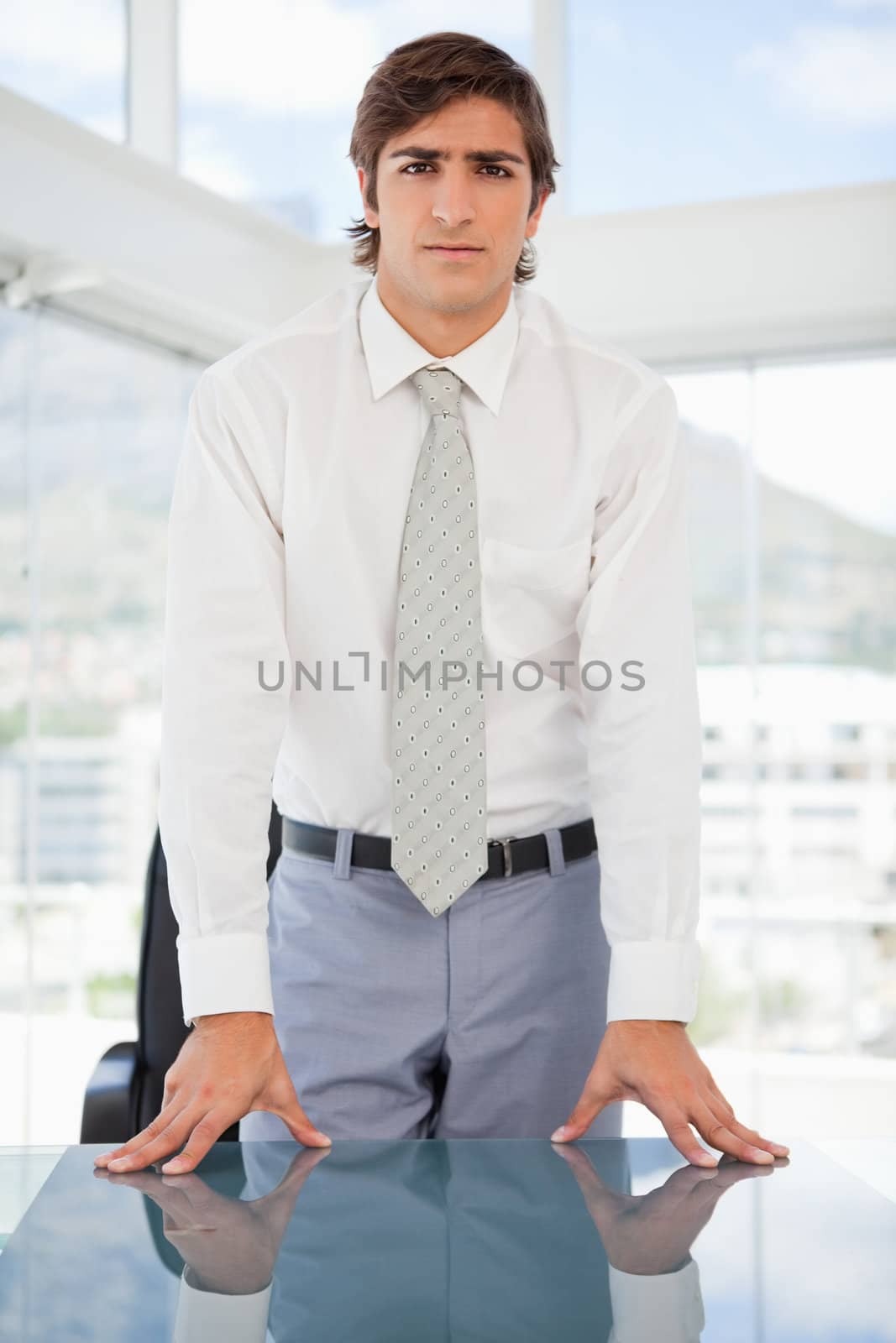 A serious businessman is leaning on a table