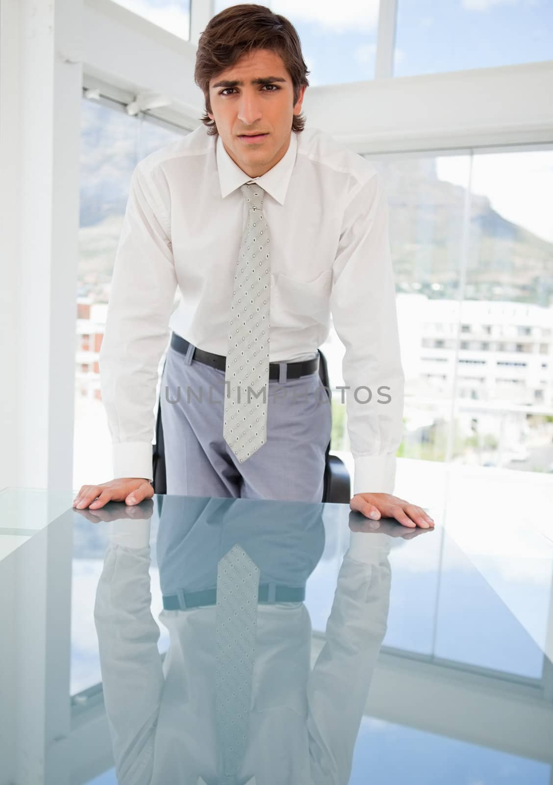Young serious businessman leaning on a table by Wavebreakmedia