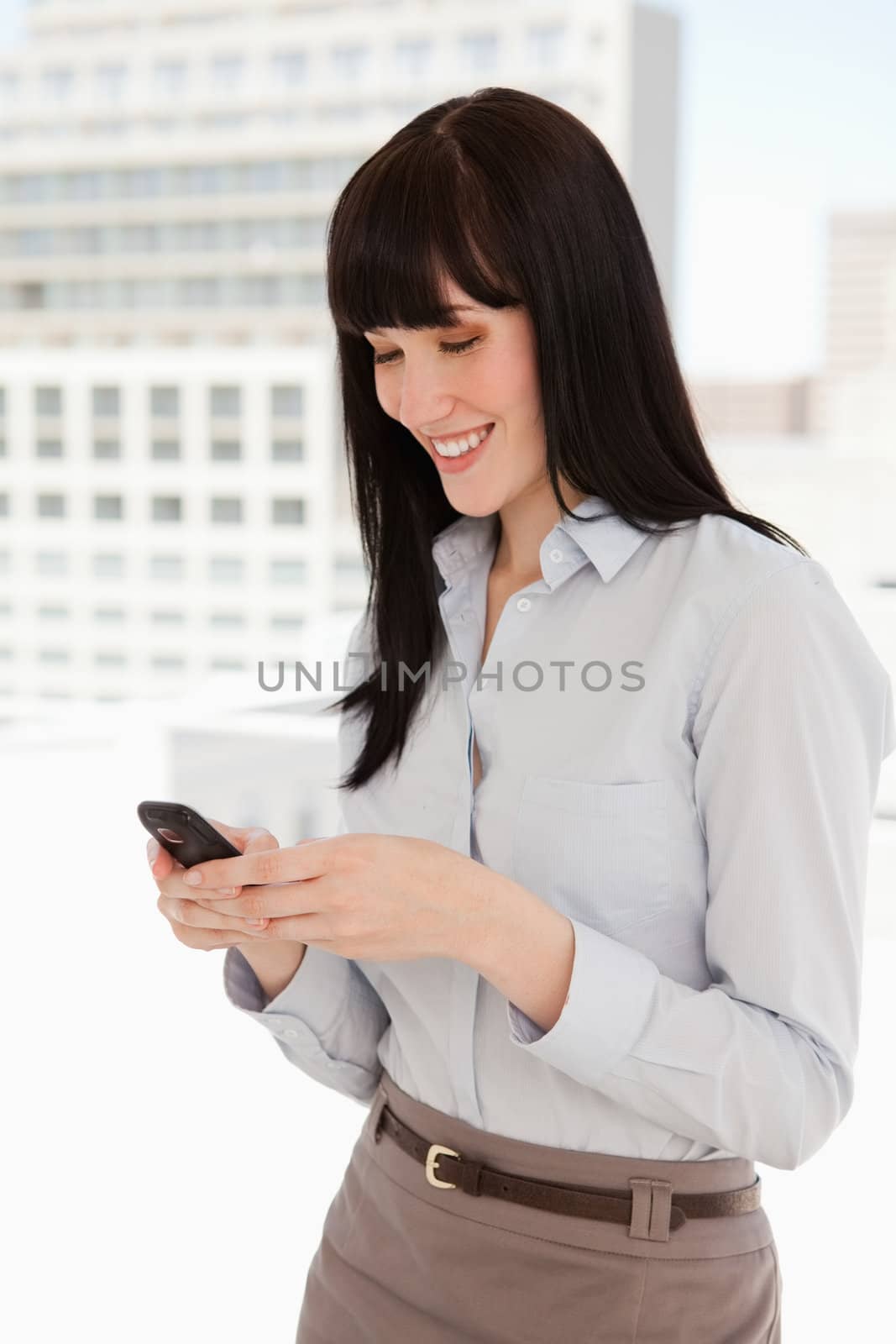 Smiling woman at work sending a text message by Wavebreakmedia