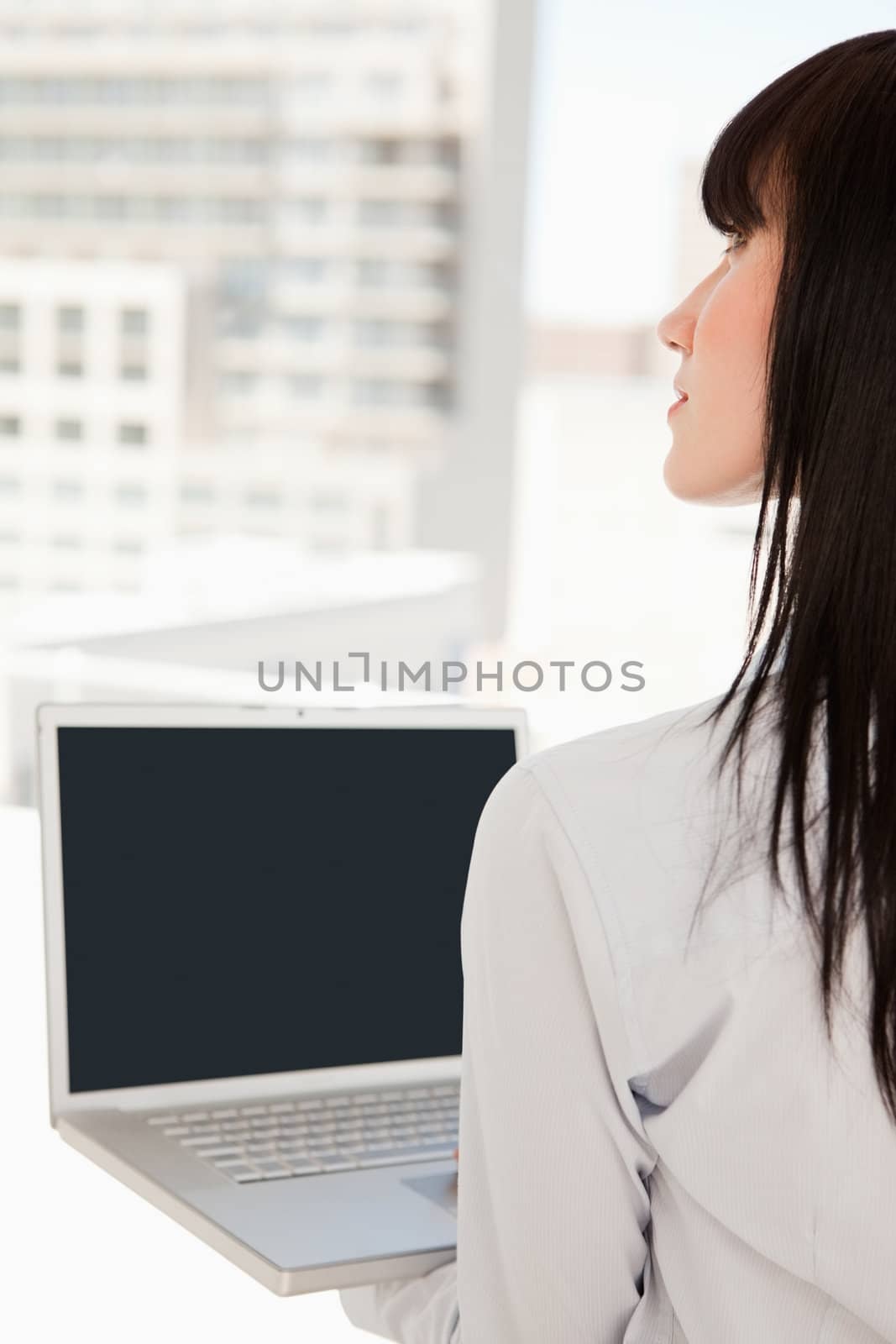A woman looking upwards in her office with a laptop in her hand