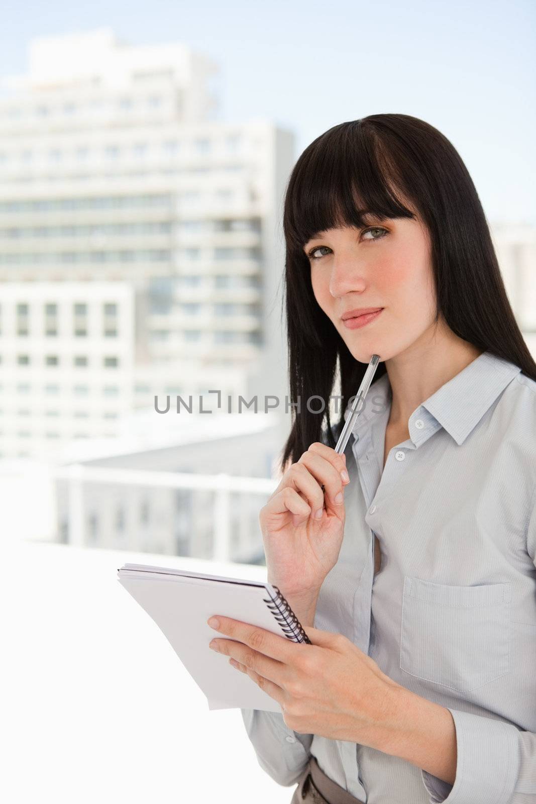 A woman with black hair looks ahead as she thinks with a notepad and pen in hand