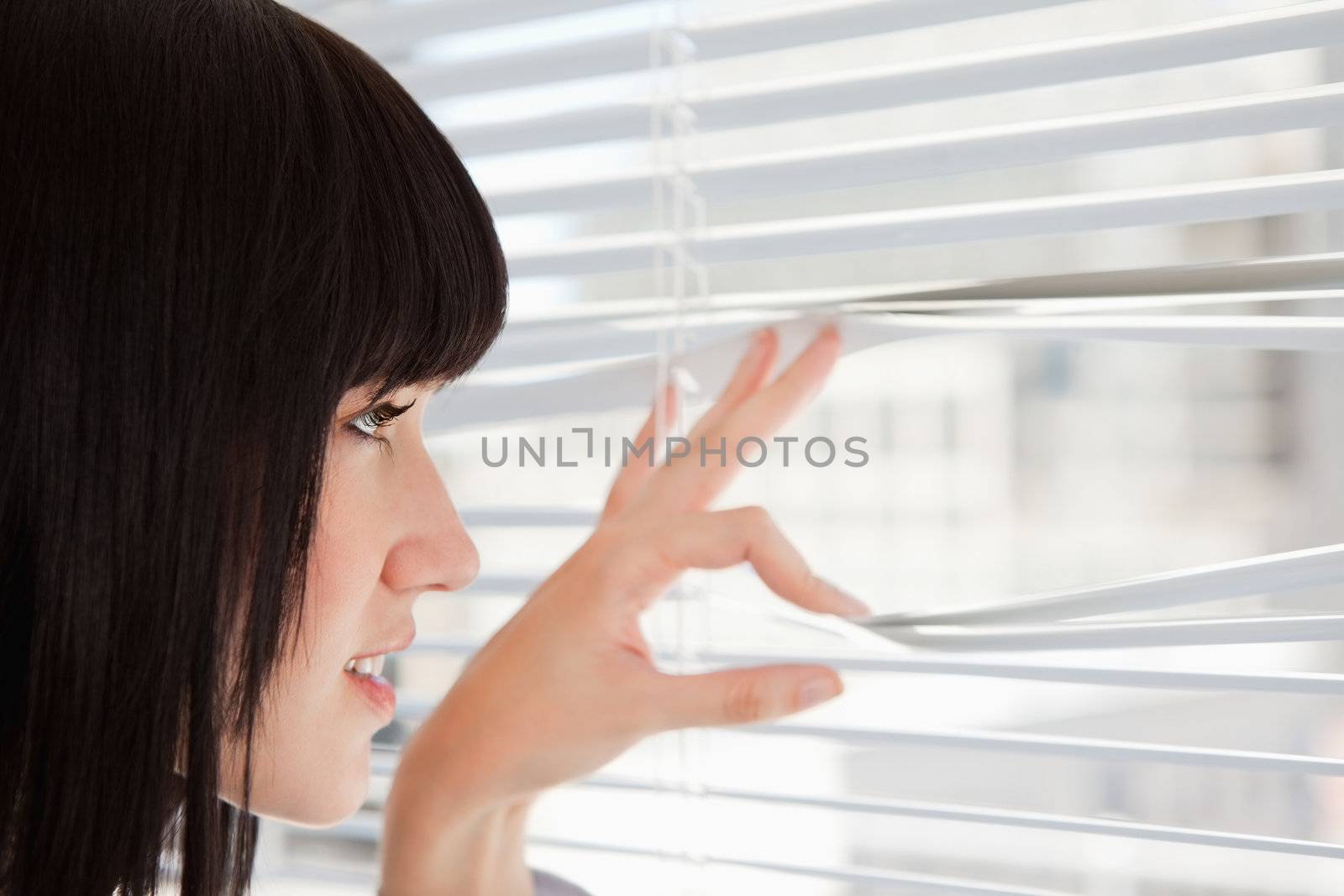 A woman at the window as she looks out through the blinds
