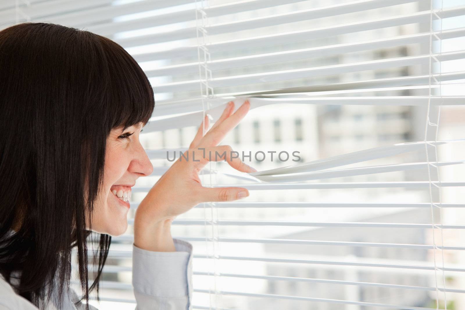 A woman smiles as she looks out through her window blinds