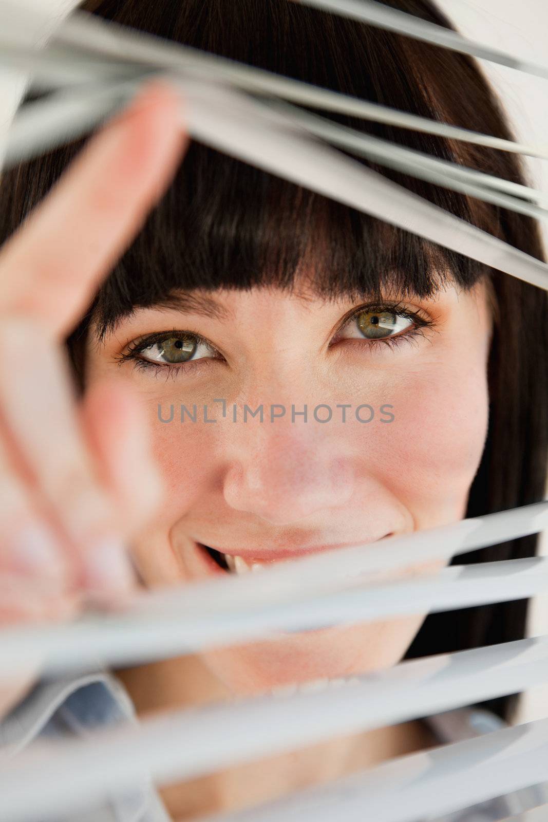 Close up of woman looking through blinds into the camera by Wavebreakmedia