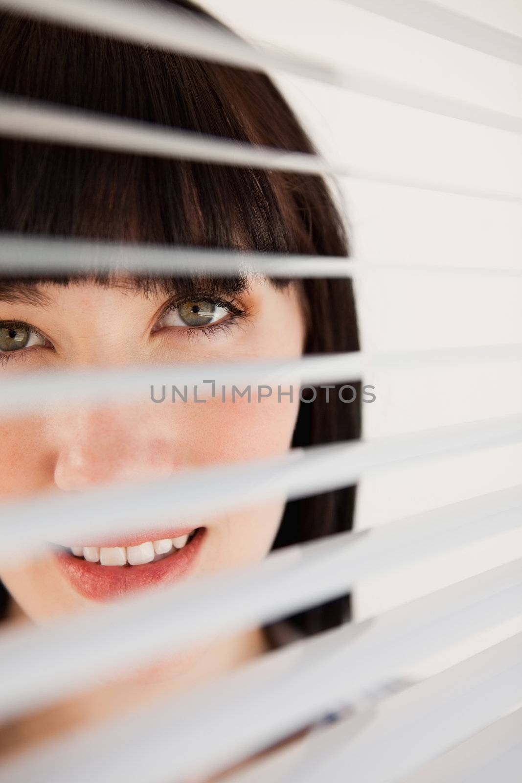 A woman looking forward through her blinds without moving them by Wavebreakmedia