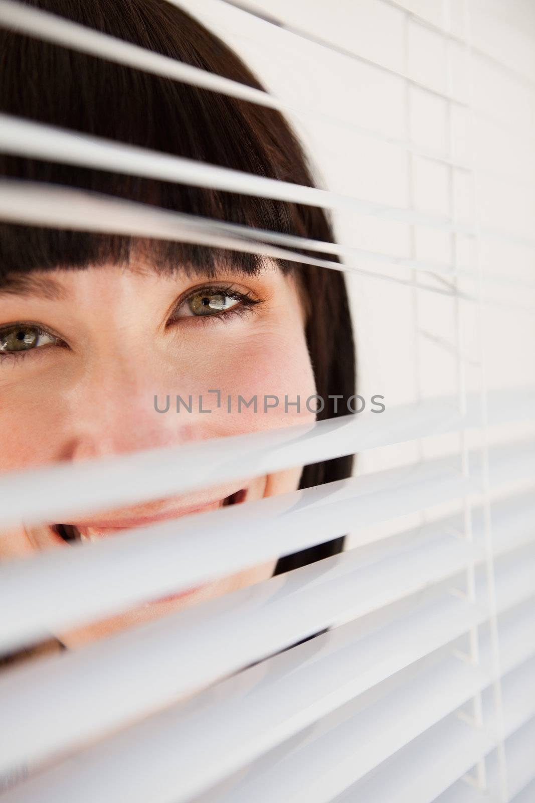 A woman looking through blinds she has opened slightly by Wavebreakmedia