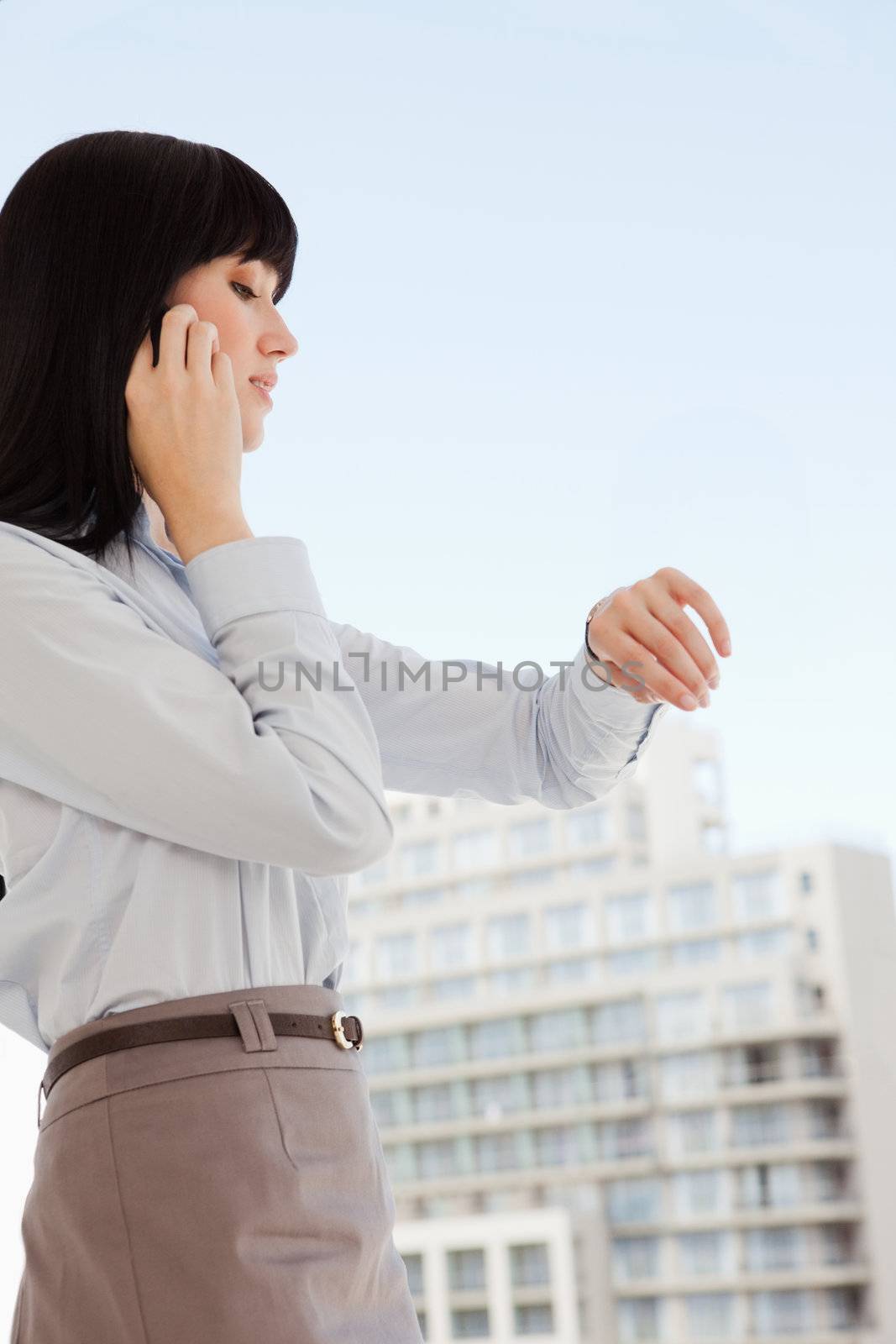 A business woman makes a phone call as she looks at the time by Wavebreakmedia
