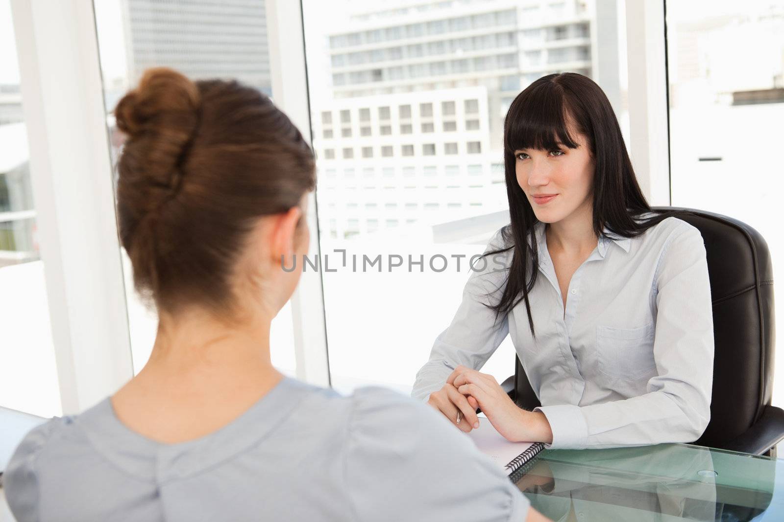 A smiling business woman listens to what the other woman has to  by Wavebreakmedia