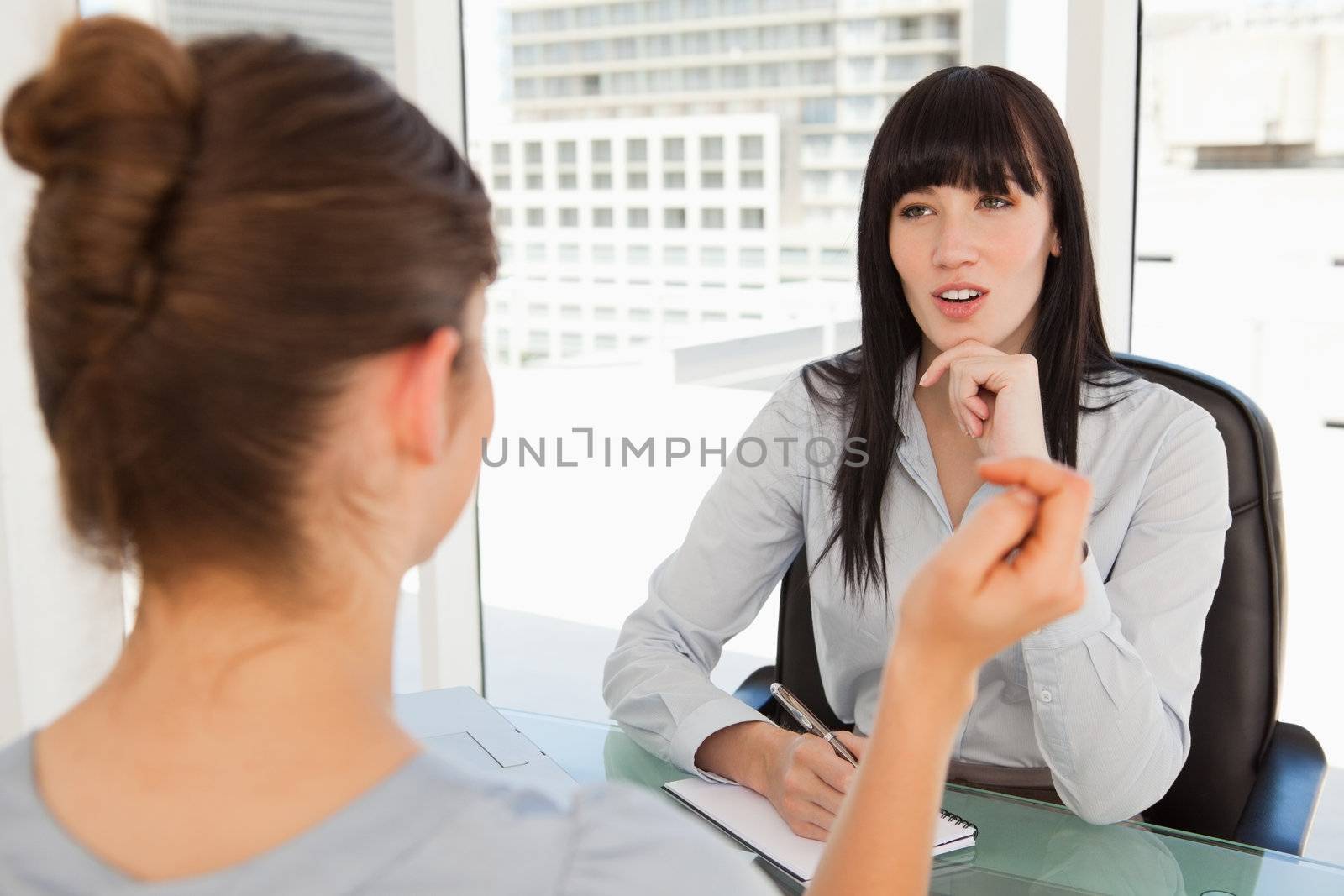 A business woman listens to the other woman in her office by Wavebreakmedia