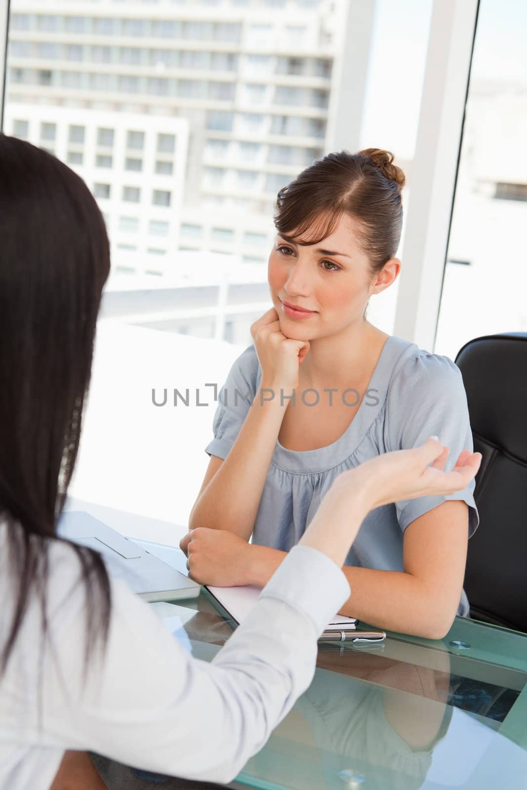 Brunette and black haired co workers chat to one another in an office
