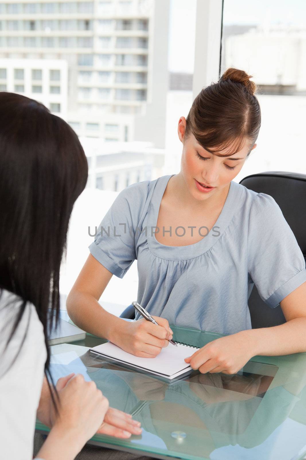 As her co-worker chats the brunette employee writes on her note  by Wavebreakmedia
