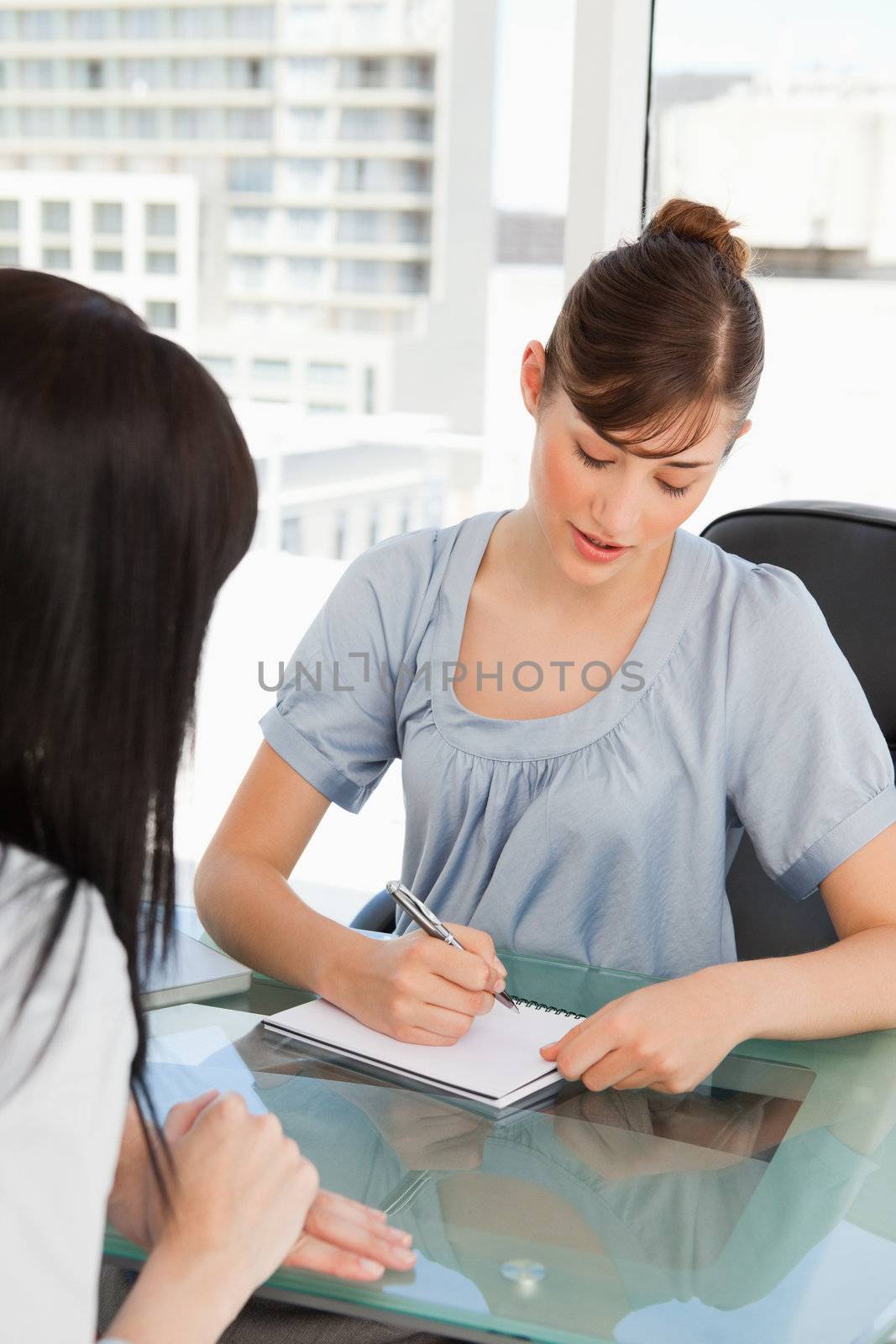 An attractive employee writes down on her pad as they other worker talks to her