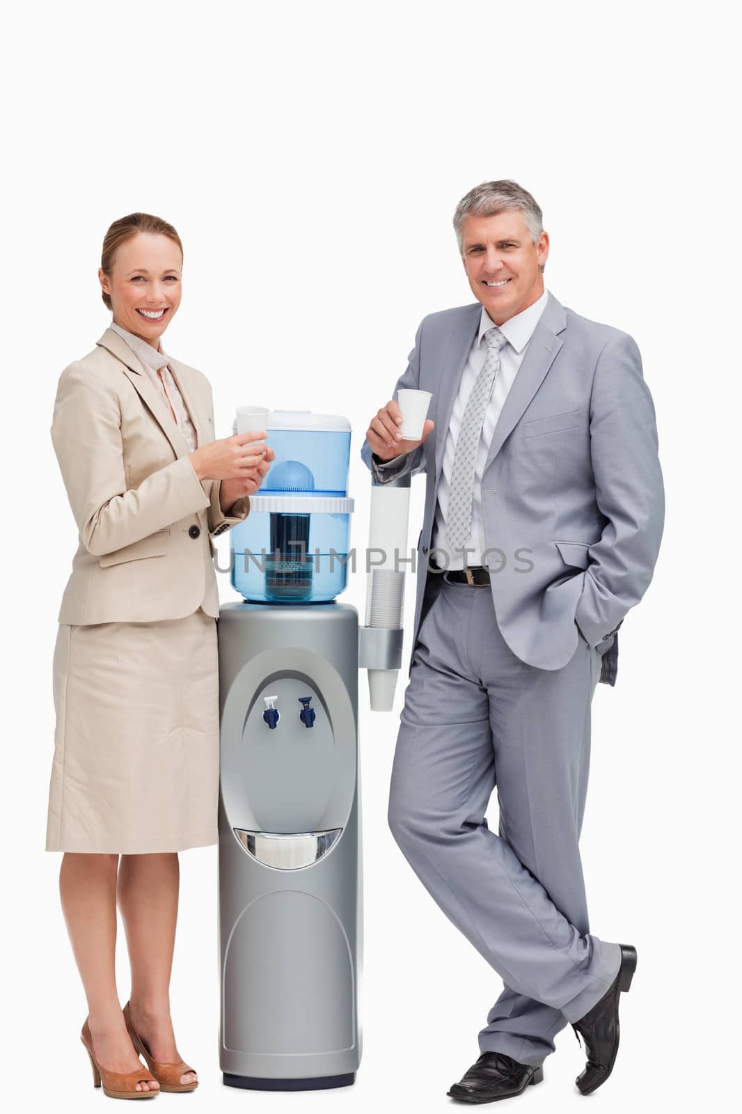 Portrait of smiling business people next to the water dispenser against white background