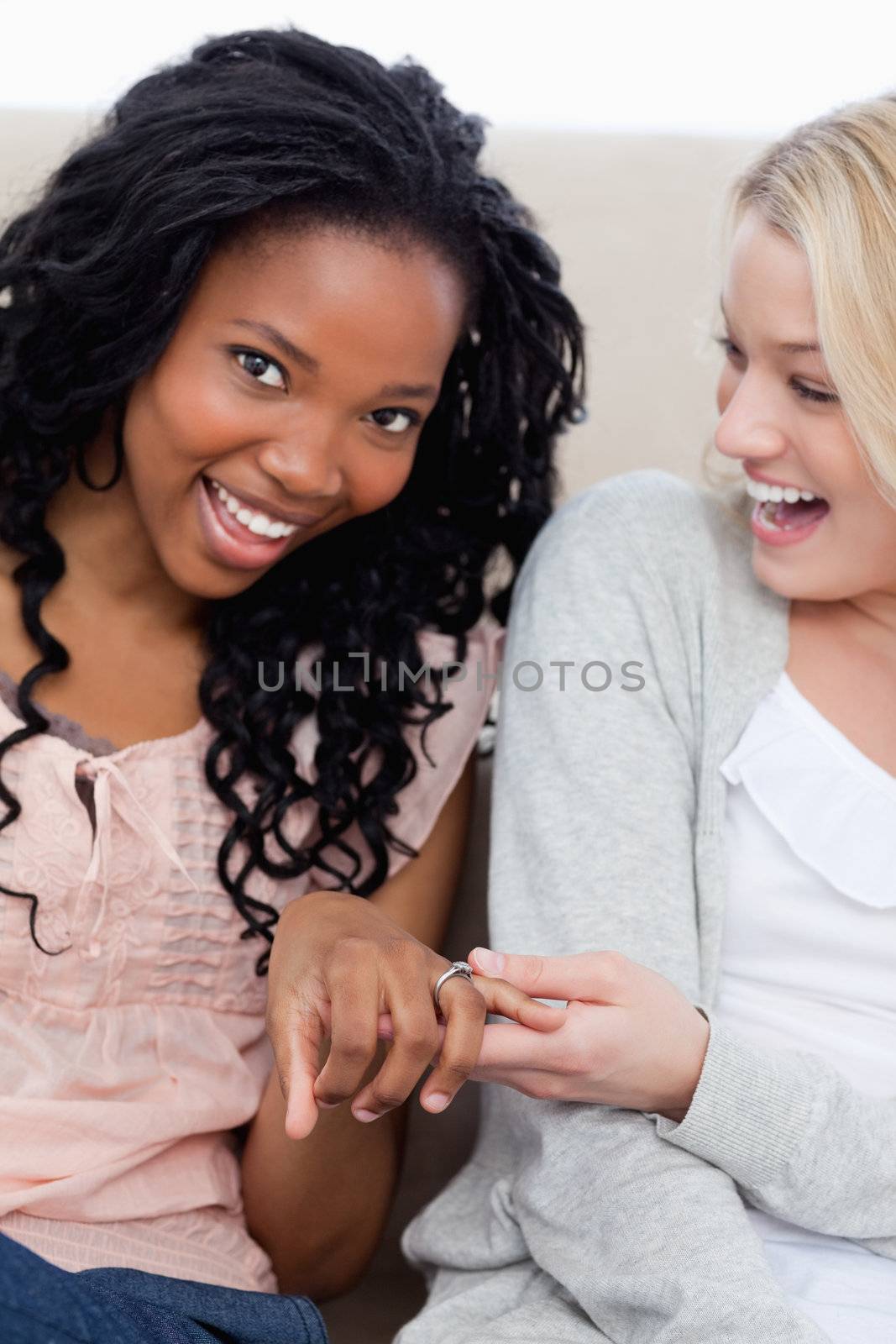 A smiling woman is looking at the camera and showing her friend her wedding ring