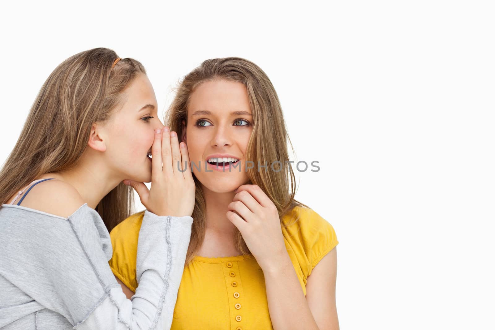 Blonde student whispering to her beautiful friend against white background