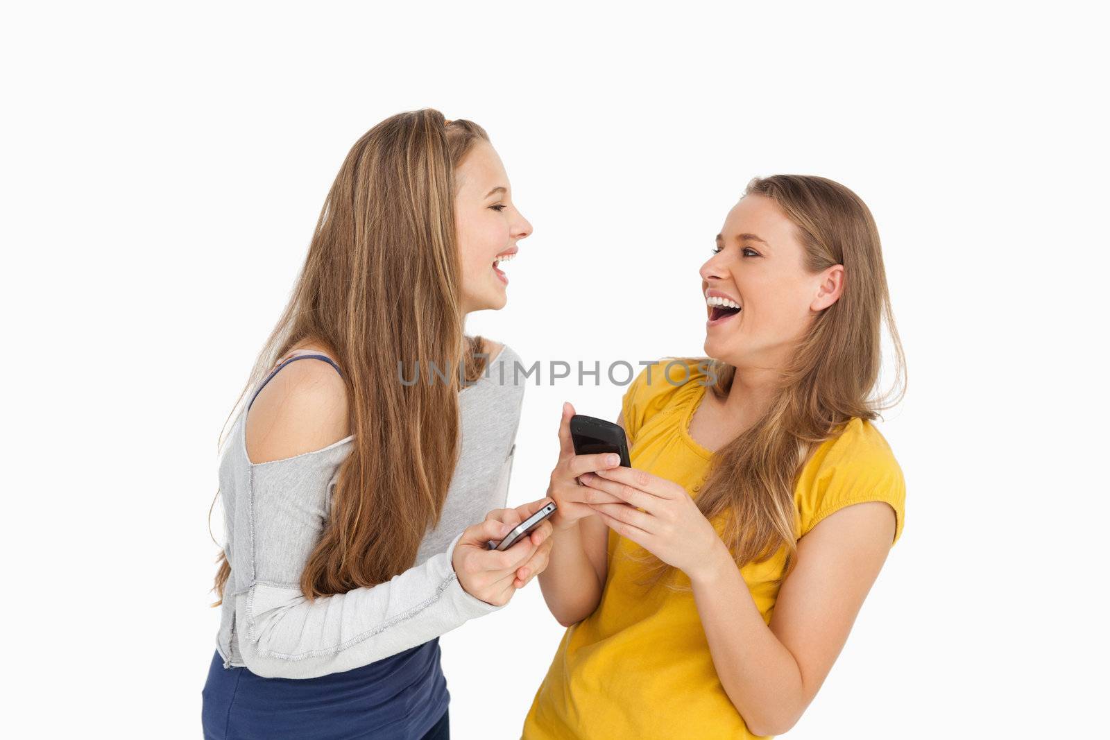 Two young women laughing while holding their cellphones against white background
