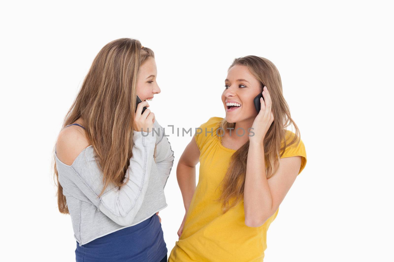 Two young women laughing on the phone together against white background