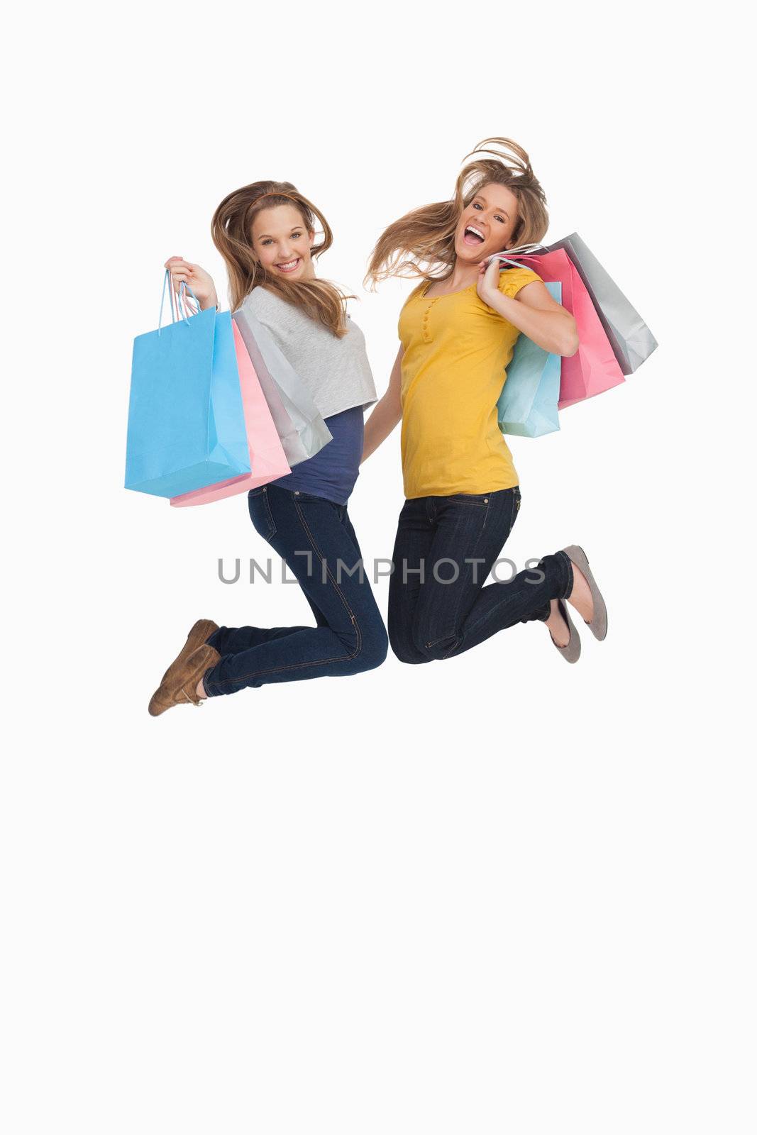 Two young women jumping with shopping bags against white background