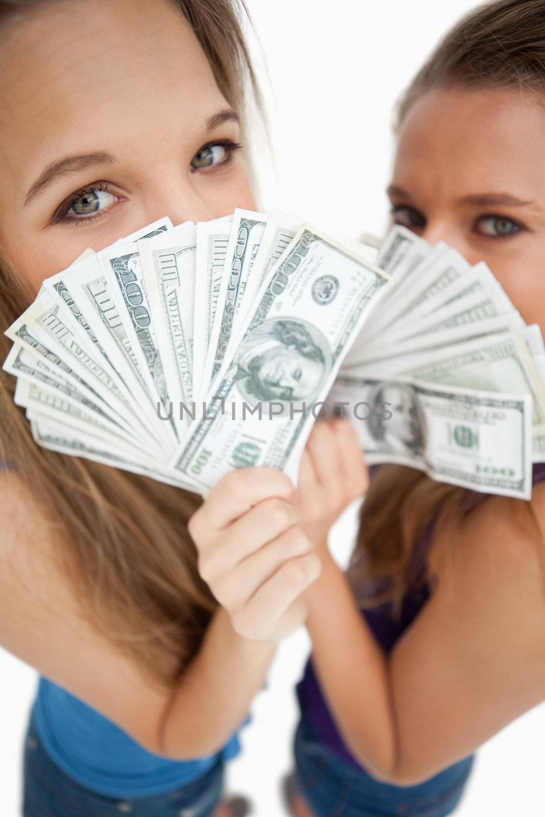 High-angle view of two young woman behind dollars against white background