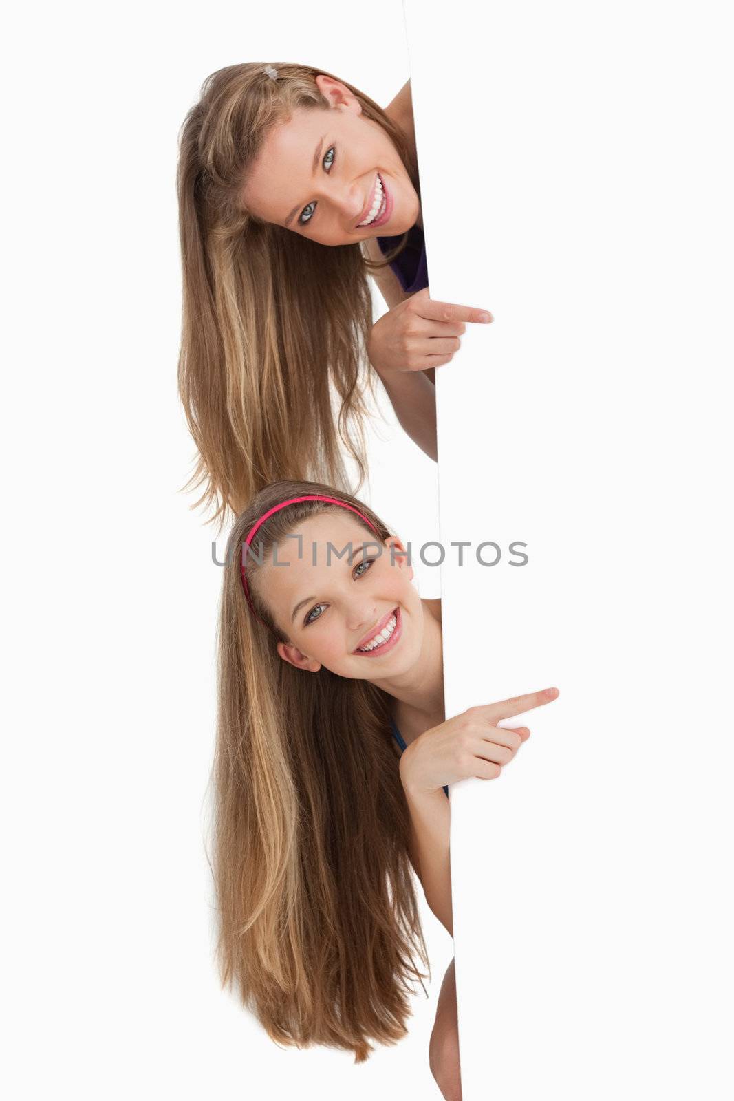 Portrait of two long hair students pointing behind a blank sign against white background