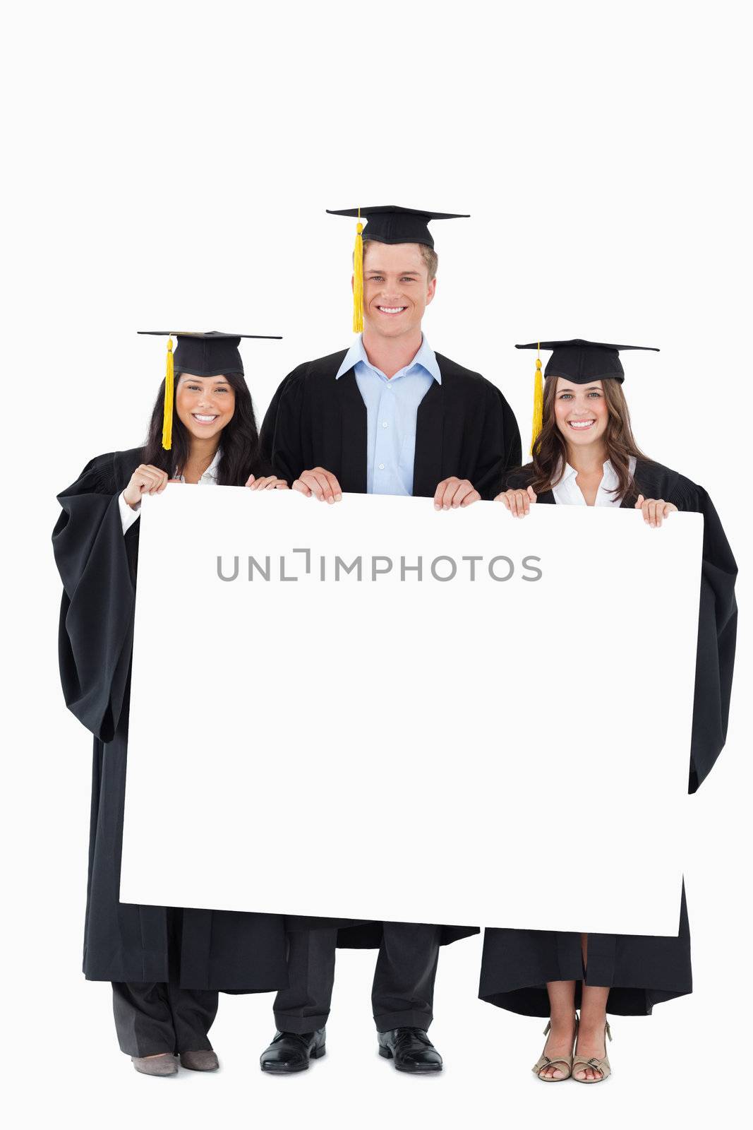 A full length shot of three graduates holding a blank poster in front of them  