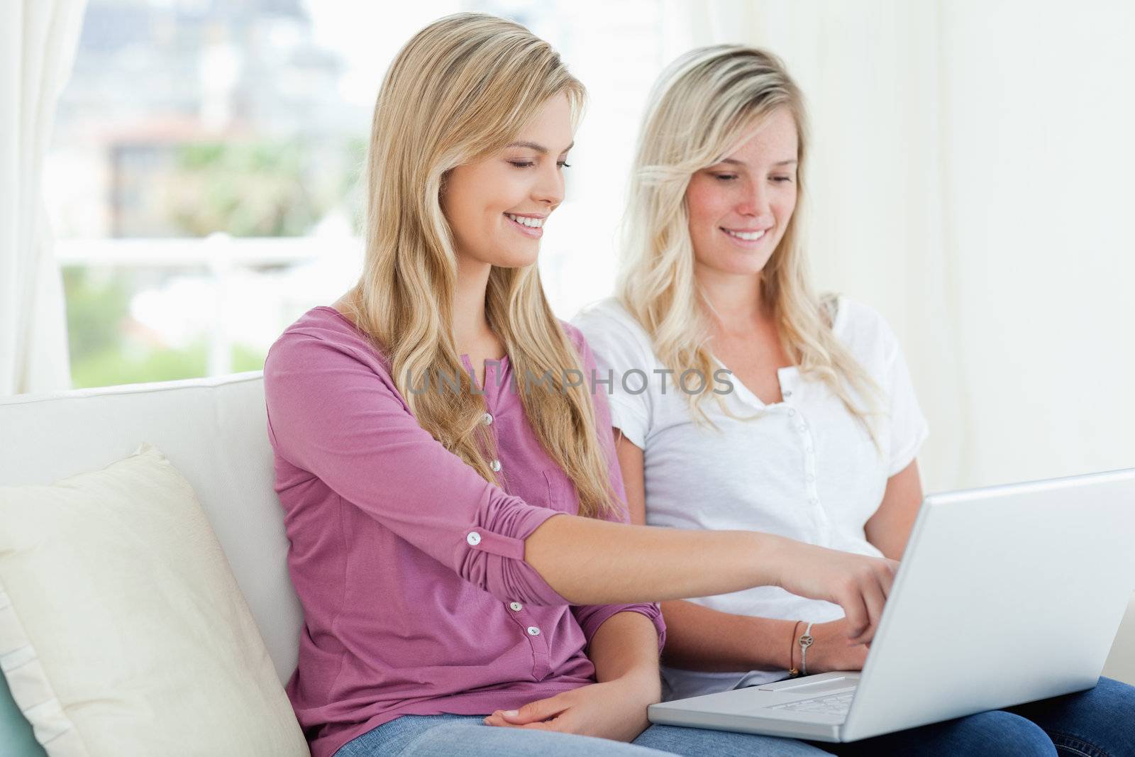 Women sitting and smiling while on the couch as they look at the laptop 