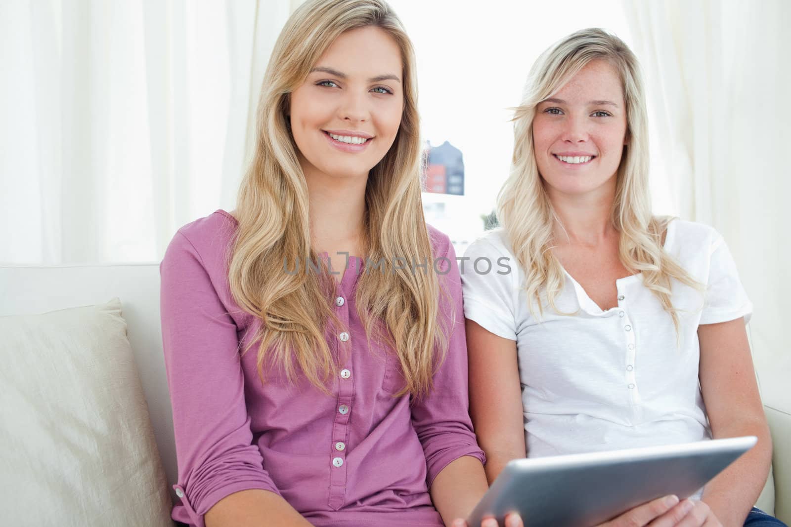 Friends sitting together with a tablet in hand as they both look at the camera 
