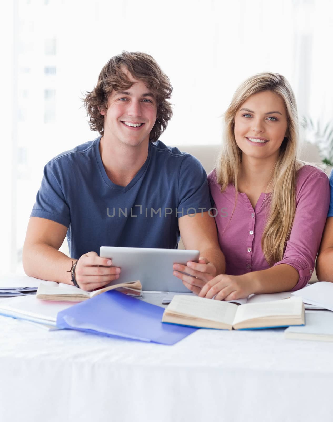 A couple hold a tablet together while looking into the camera by Wavebreakmedia