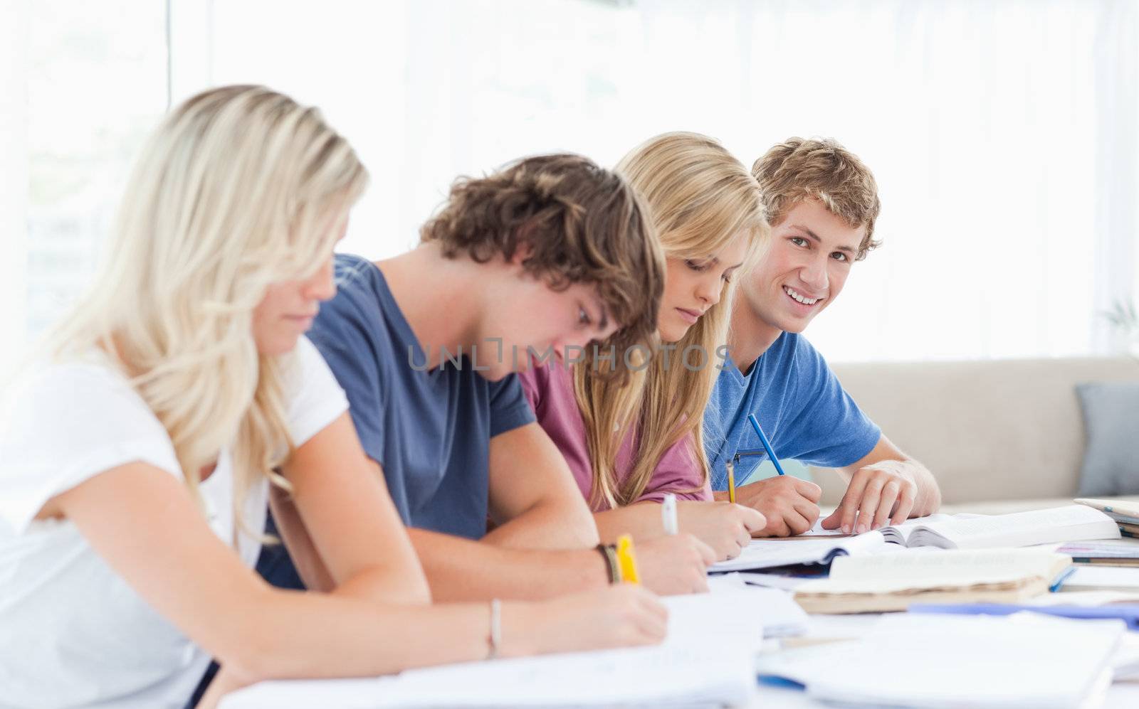 A group of students working as one student looks at the camera w by Wavebreakmedia