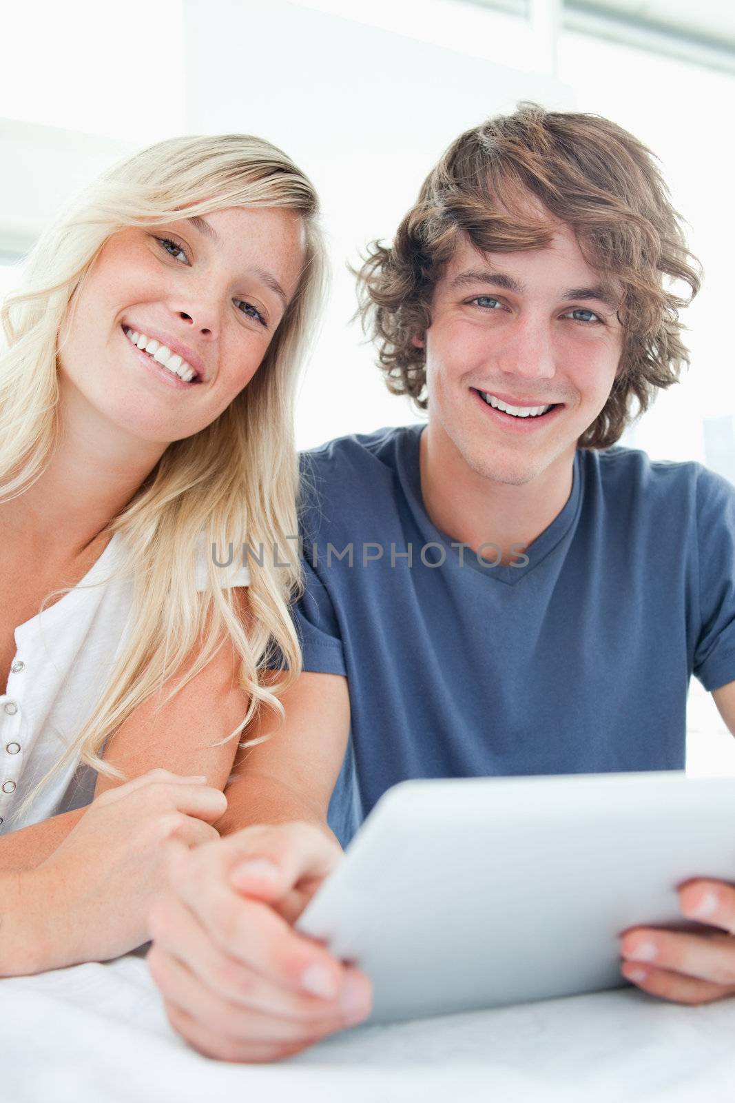 A smiling couple holding a tablet and looking at the camera while they sit together