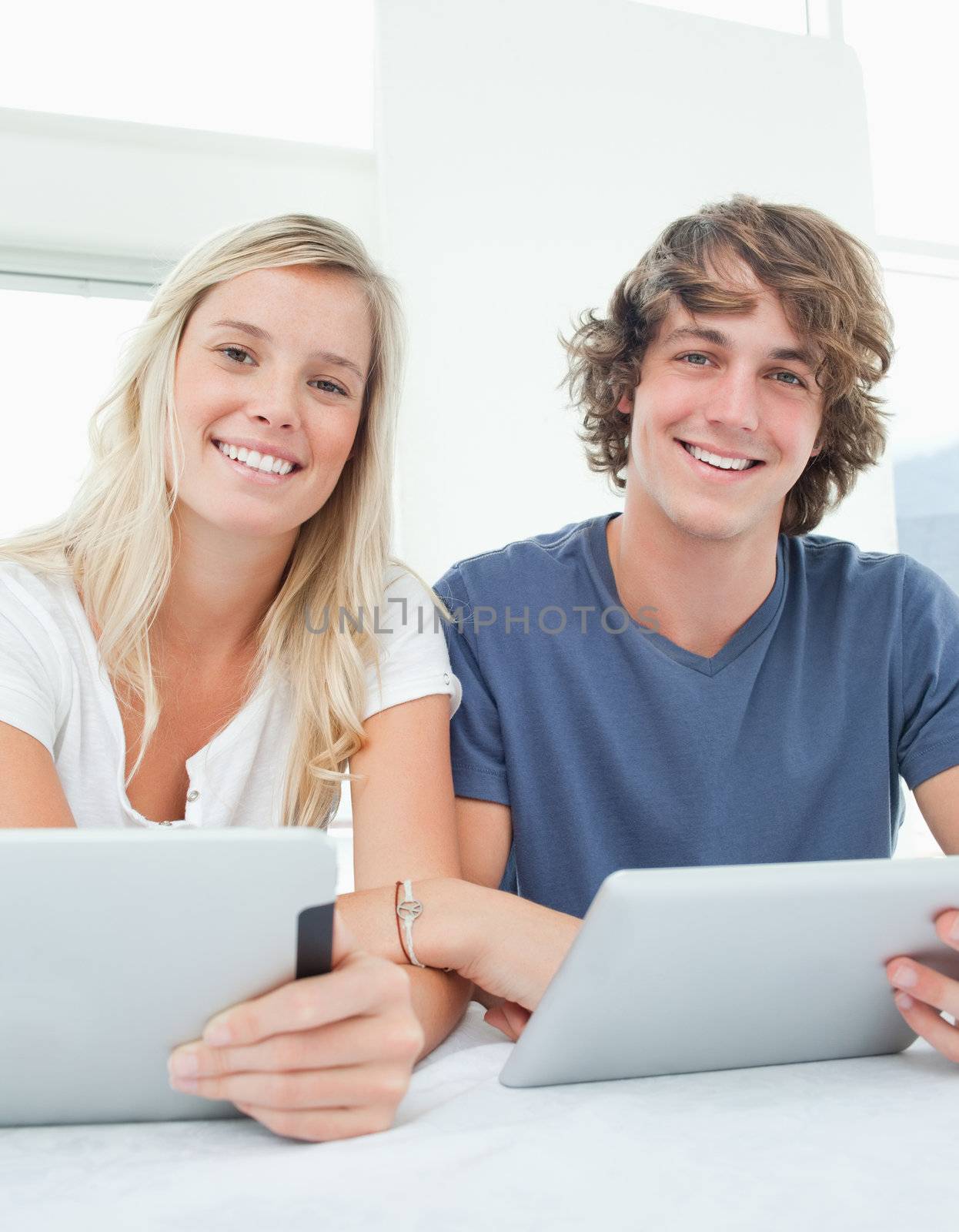 A smiling couple looking at the camera as they both hold tablets 