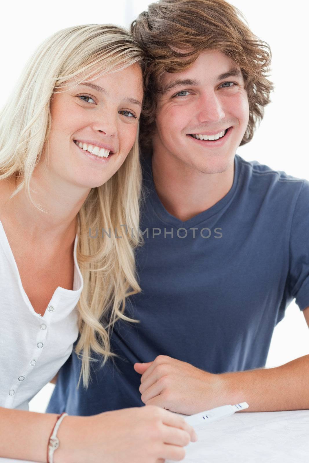 A couple looking at the camera as they smile while holding a pregnancy test 