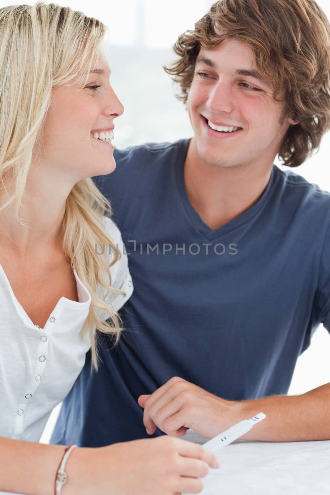 A smiling couple looking at one another as they hold a pregnancy by Wavebreakmedia