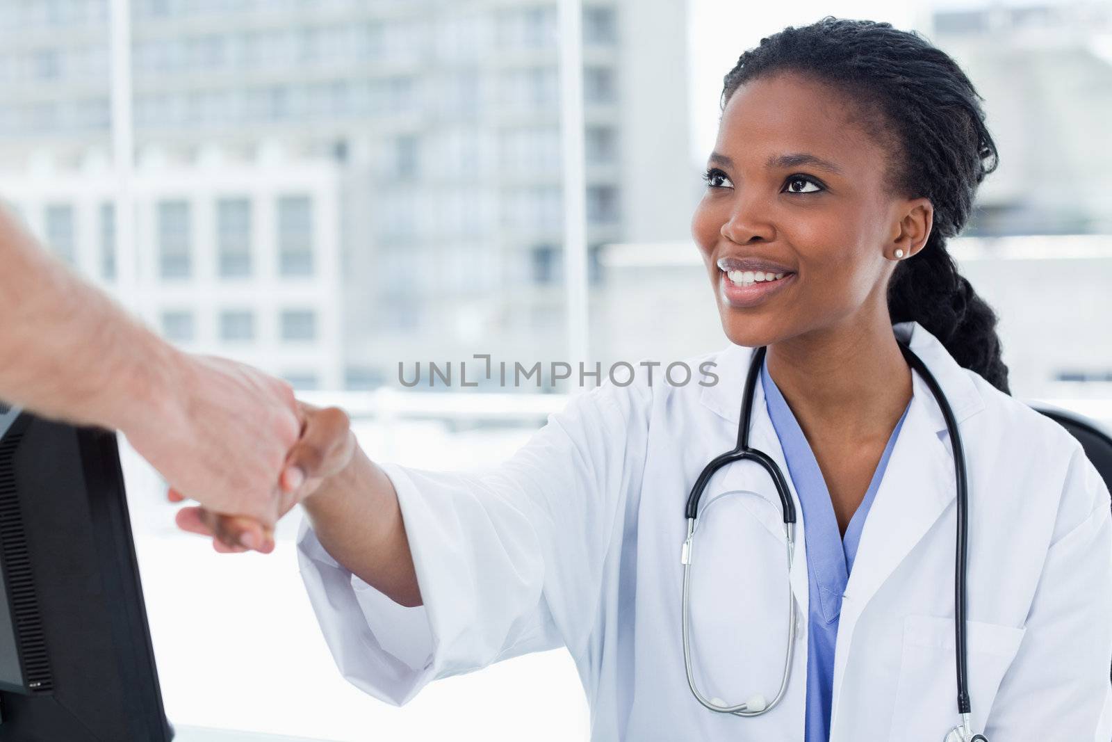 Female doctor shaking a hand in her office
